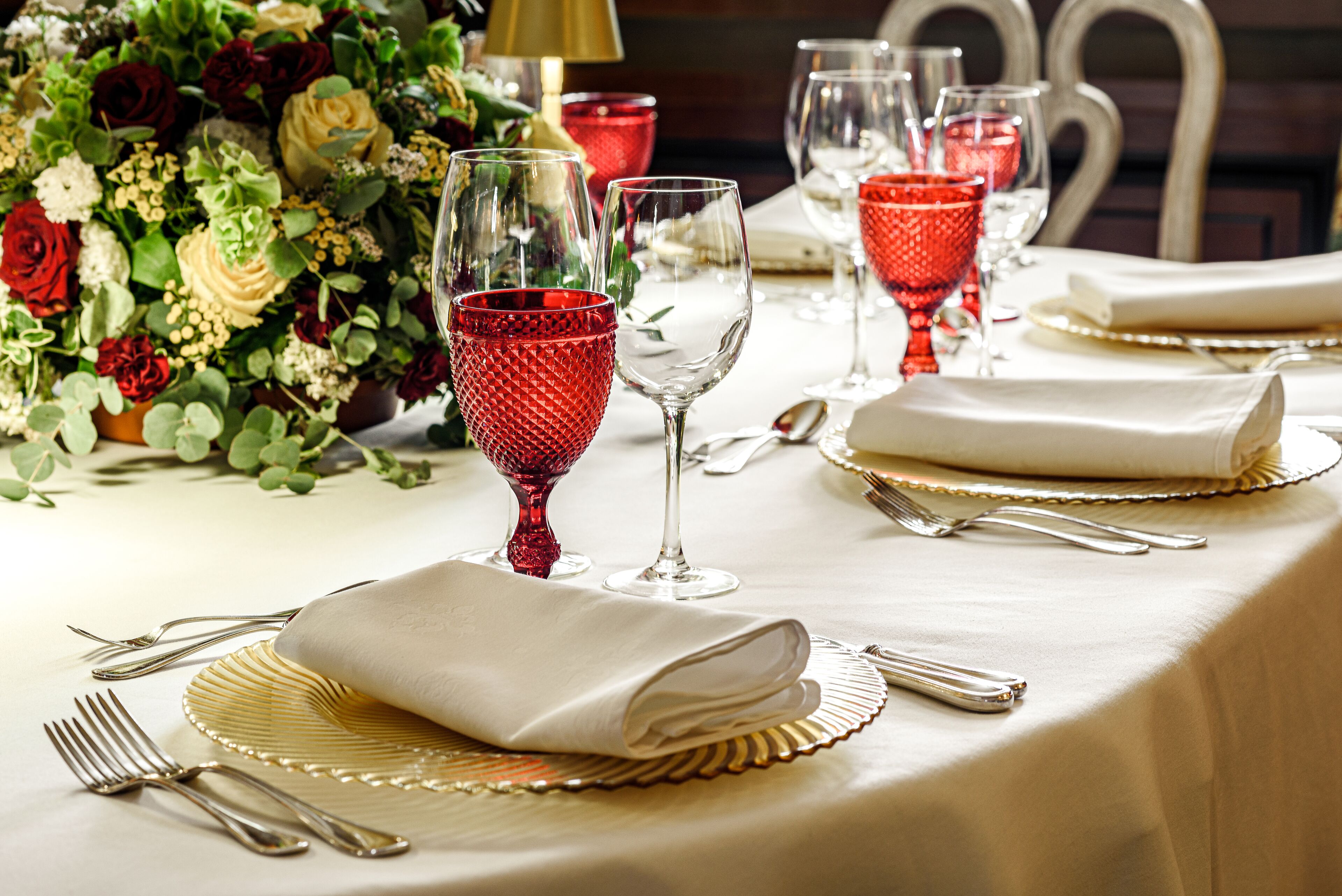A table set with red glassware, white napkins, and gold-rimmed plates.