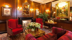 Un hall d’entrée luxueux avec un fauteuil rouge, un canapé, une cheminée et un grand miroir.