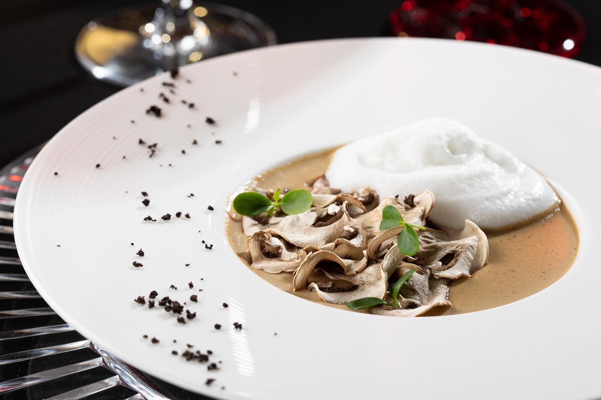 A white plate with a creamy mushroom dish, a dollop of white cream, and some green leaves.