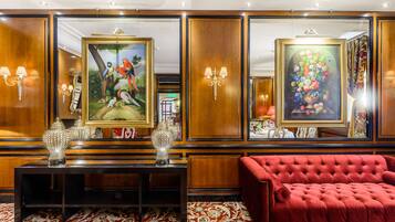 Um hall luxuoso com um sofá vermelho, uma mesa de consola de madeira com vasos decorativos e duas grandes pinturas emolduradas.