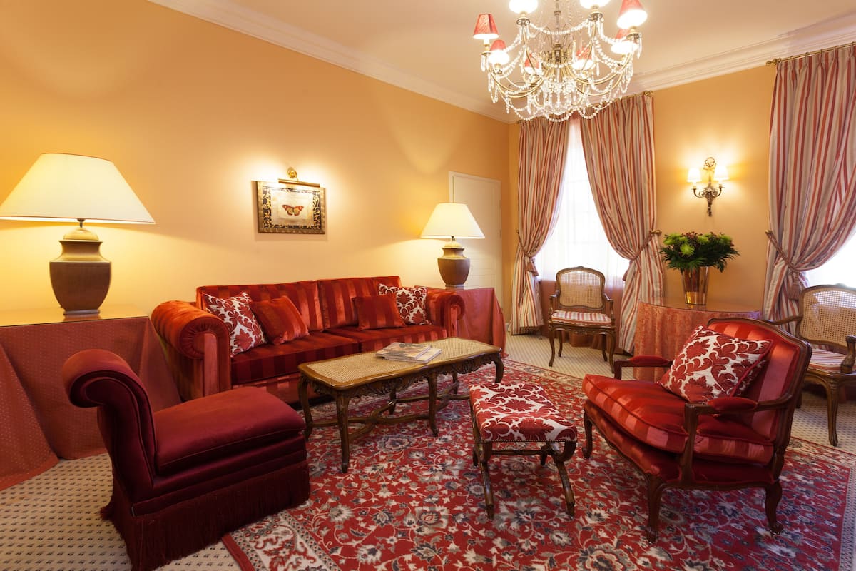 Una sala de estar con un sofá rojo, sillones, una mesa de centro y una araña.
