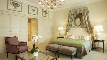 A hotel room with a large bed, a sitting area with a chair and ottoman, a glass coffee table, and a chandelier.