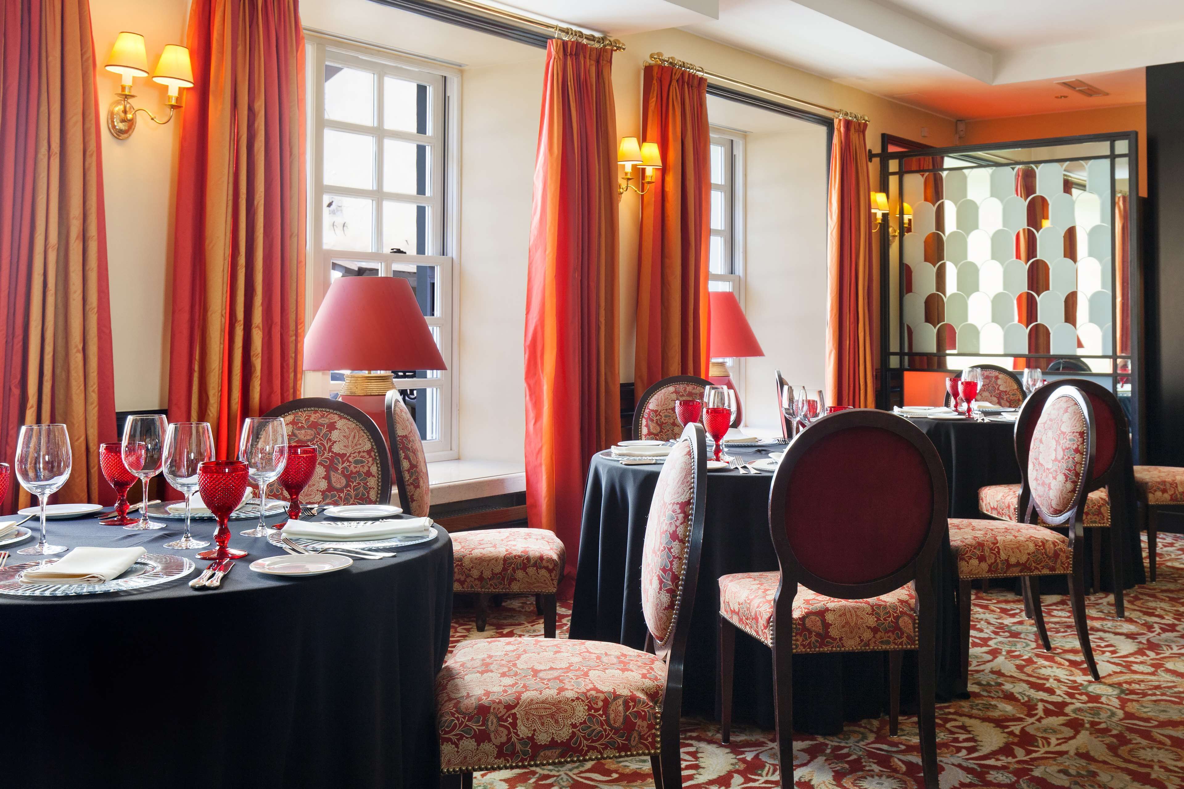 A dining area with round tables, red upholstered chairs, and red table settings.