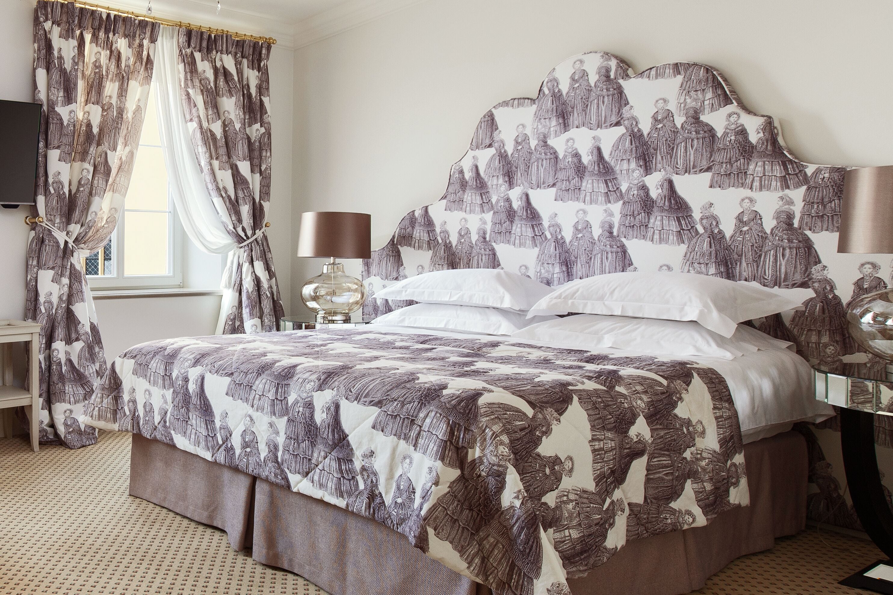 A bedroom with a large bed, a nightstand, a lamp, and a window with curtains.