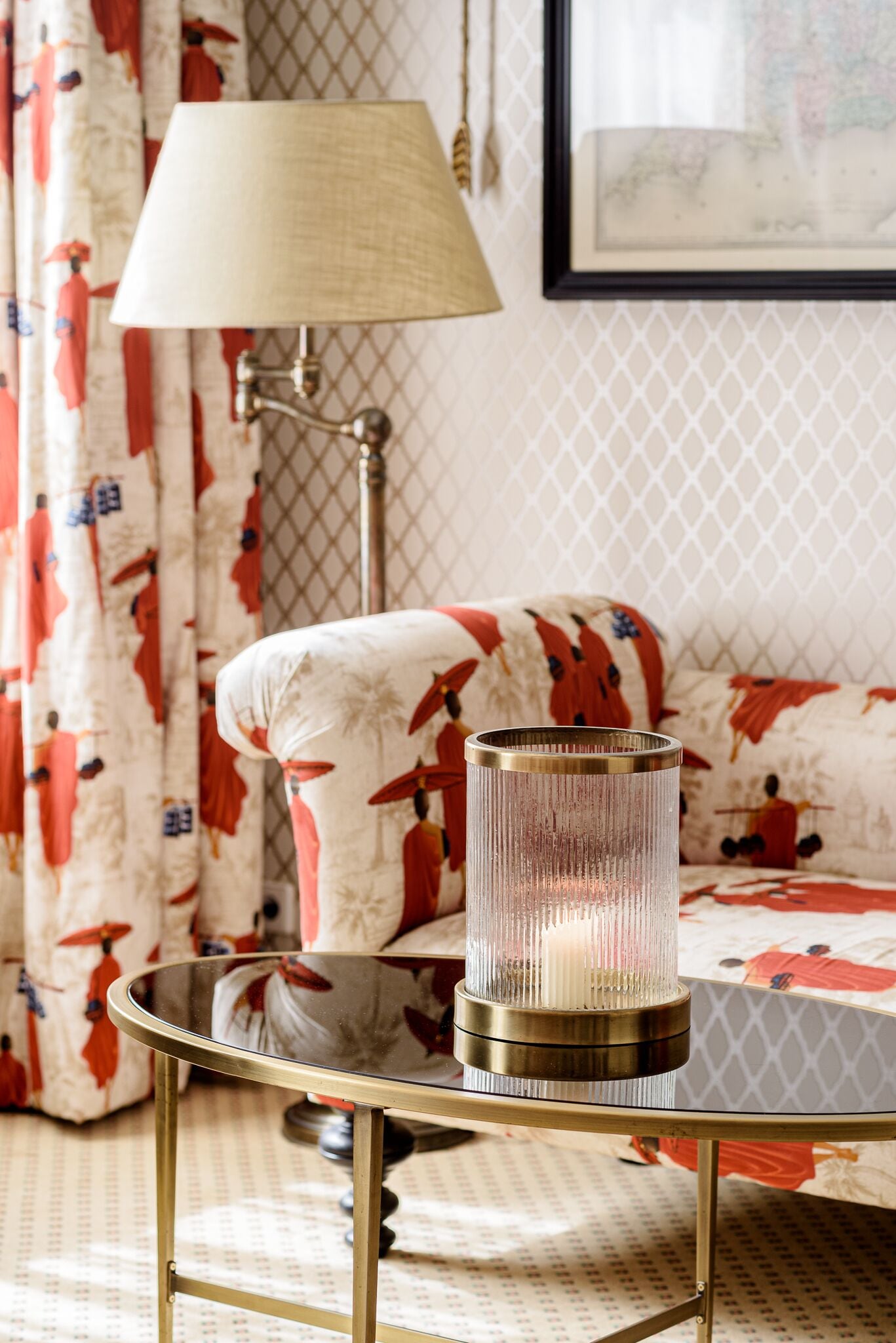 A room with a round glass table, a lamp, and a sofa with patterned upholstery.