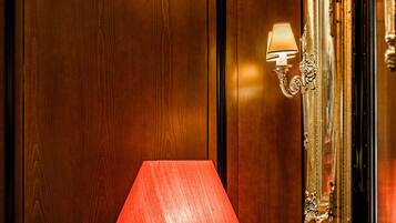 Un mur recouvert de panneaux de bois, une lampe rouge, une petite table avec un coussin et un miroir avec un cadre doré.