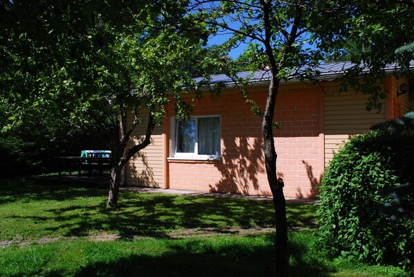 Um edifício de tijolos com janela e porta, cercado por árvores e grama.