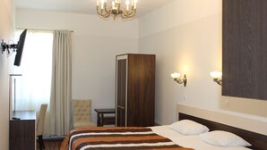 A hotel room with a bed, a desk, a chair, a wardrobe, and a chandelier. - Ecoland Hotel (Tallinn)