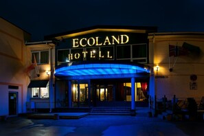 The exterior of the Ecoland Hotel with a prominent illuminated sign, a covered entrance, and a flag on the right side. - Ecoland Hotel (Tallinn)