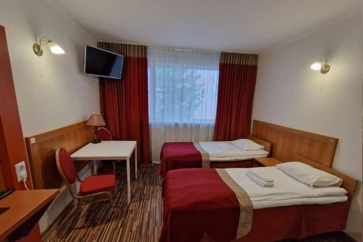 A hotel room with two beds, a desk, a chair, a TV, and a window with curtains.