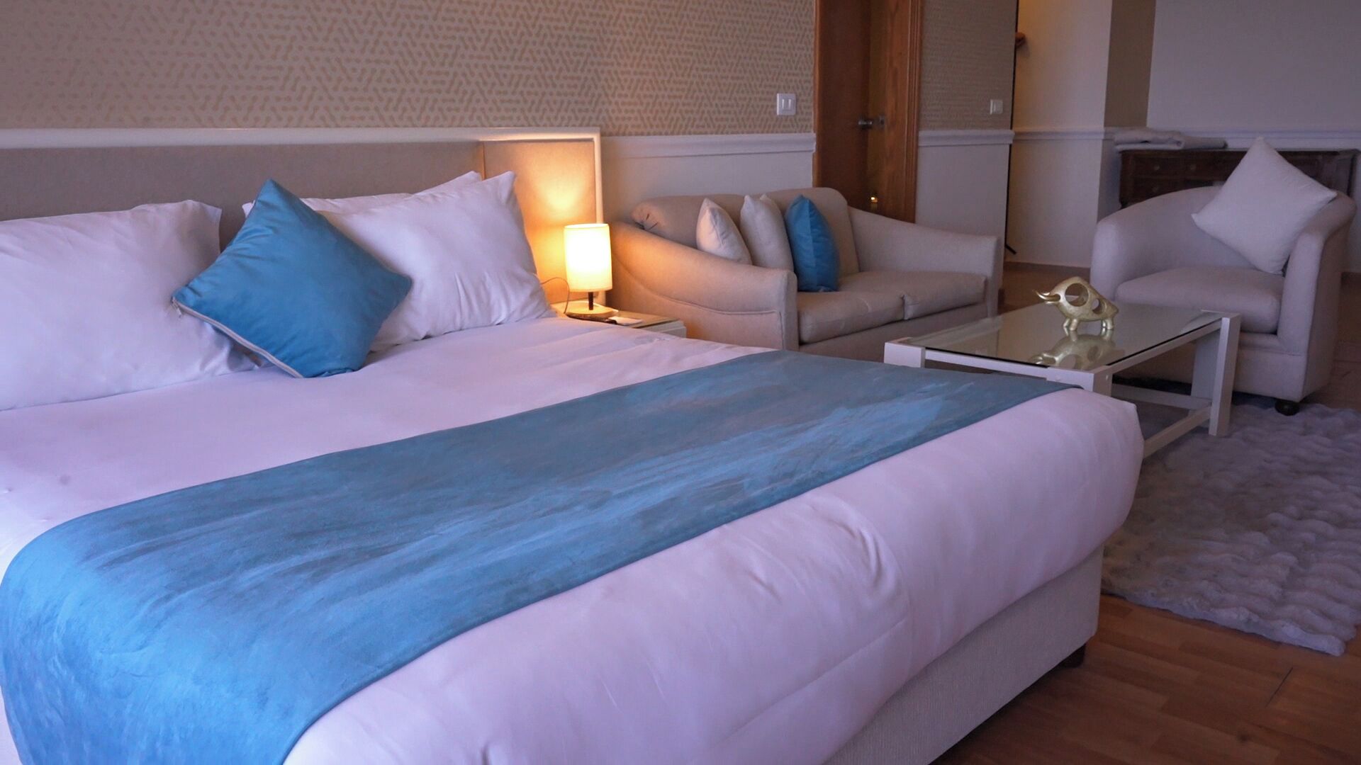 A hotel room with a large bed, a sofa, a chair, and a small table.
