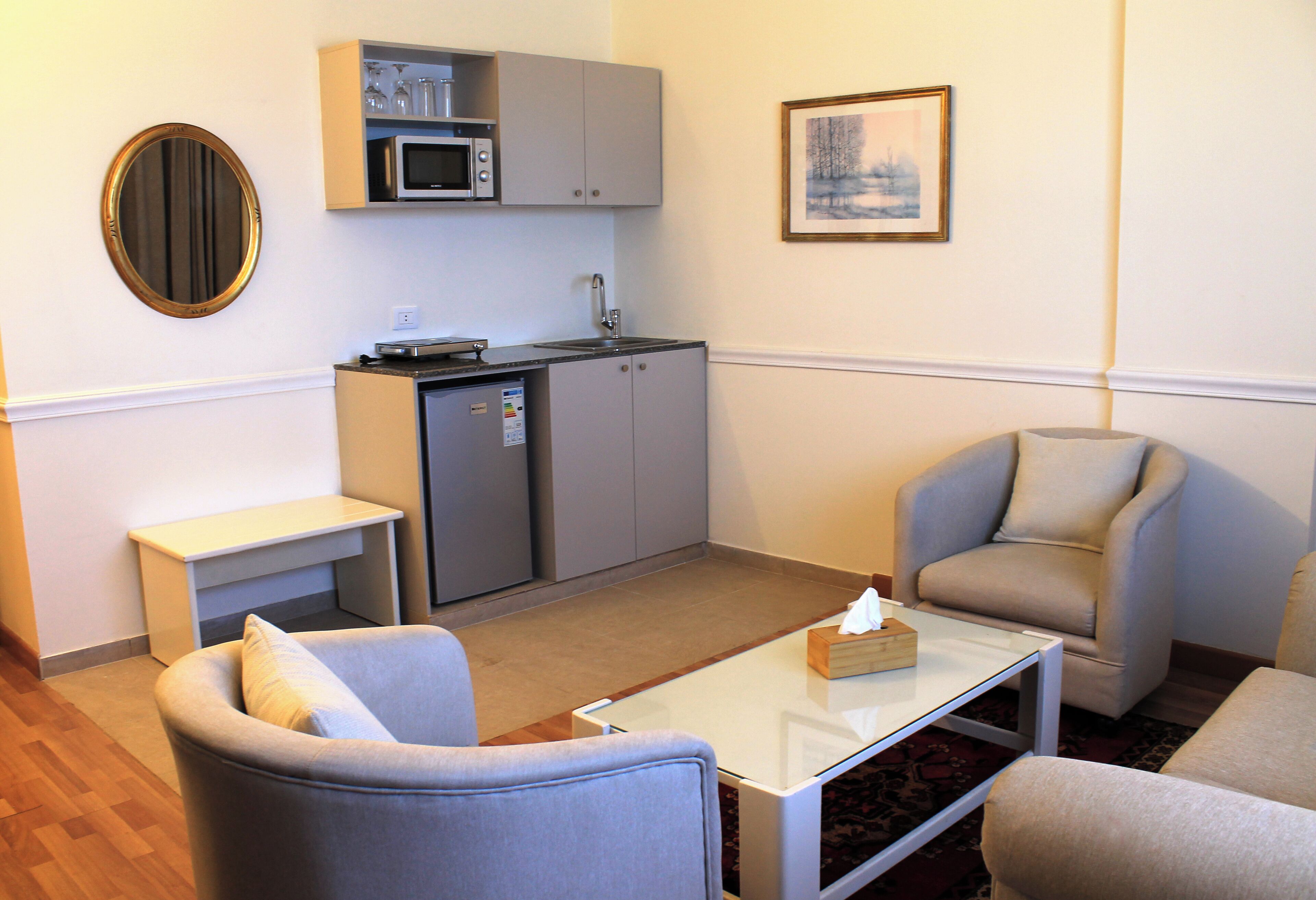 A compact living space with a kitchenette, two armchairs, a coffee table, and a framed picture on the wall.