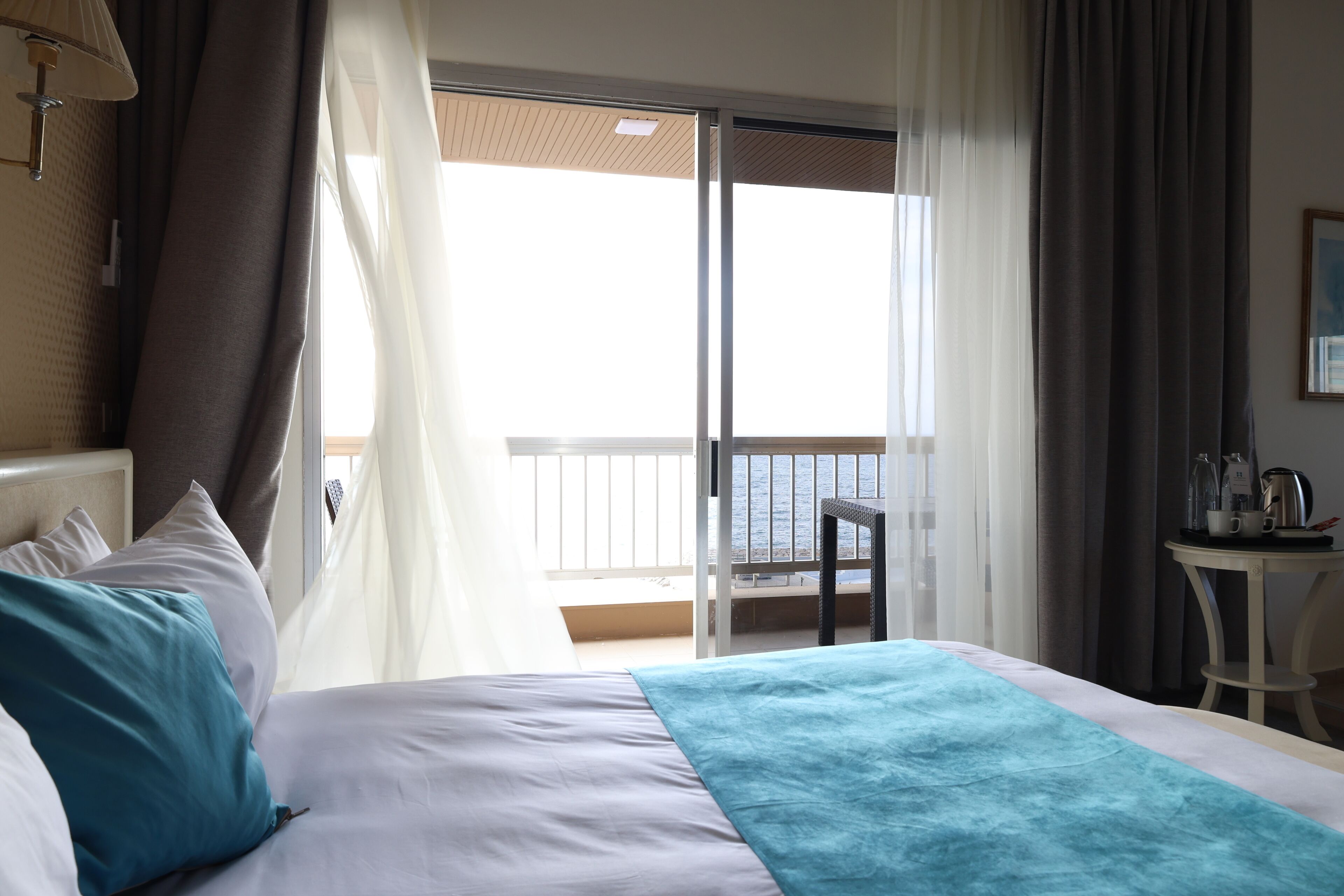 Una habitación de hotel con una cama, una mesita con una tetera y vistas al mar a través de un ventanal corredero.