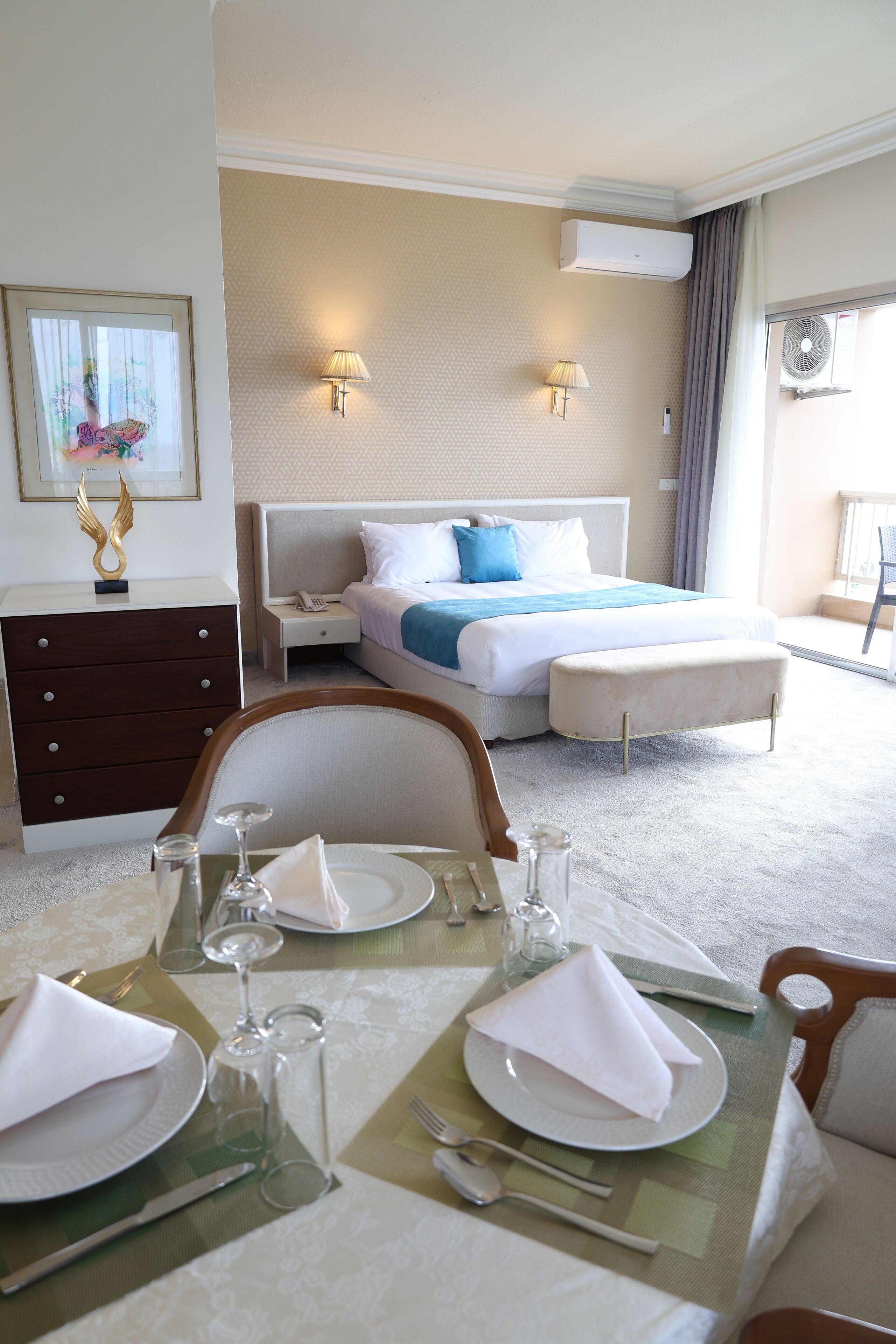 Une chambre d’hôtel avec un lit soigneusement fait, une table à manger dressée pour deux personnes et un petit bureau avec une chaise.