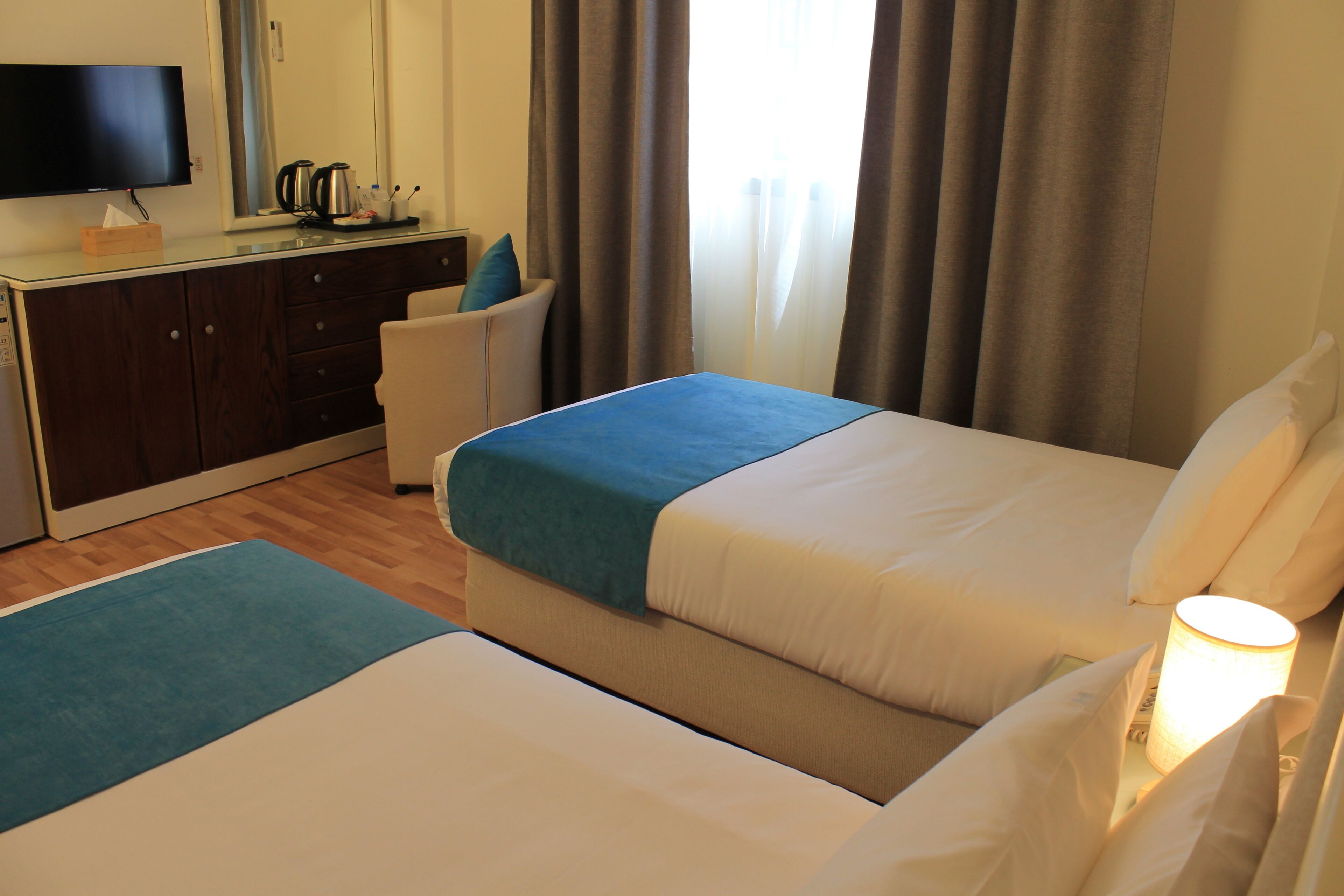 A hotel room with two beds, a desk with a television, and a window with curtains.