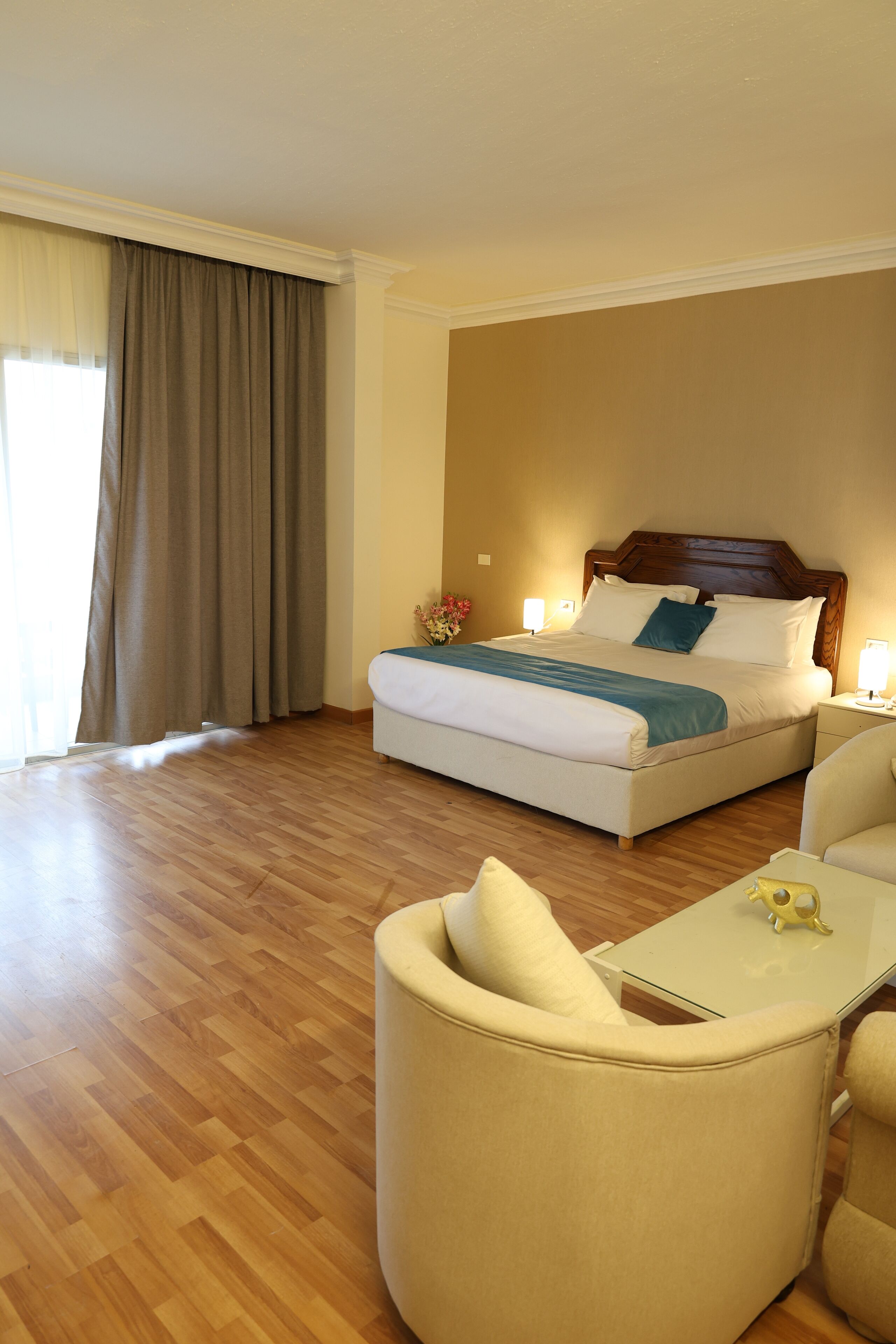 A hotel room with a bed, a chair, a small table, and a window with curtains.