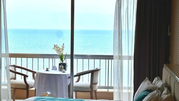 A hotel room with a balcony, a bed with a teal bedspread, a small round table with chairs, and a vase of flowers. - Hotel Méditerranée Beyrouth  (Beirut)
