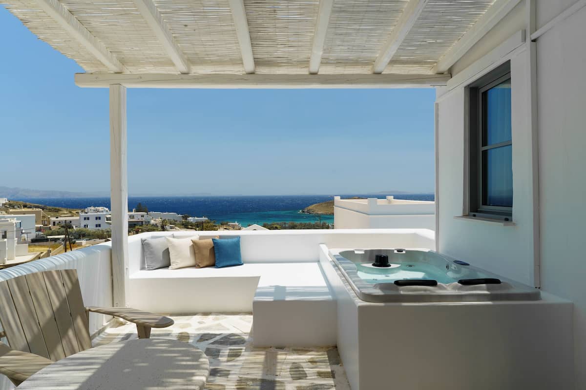 A balcony with a white sofa, a wooden chair, and a hot tub.