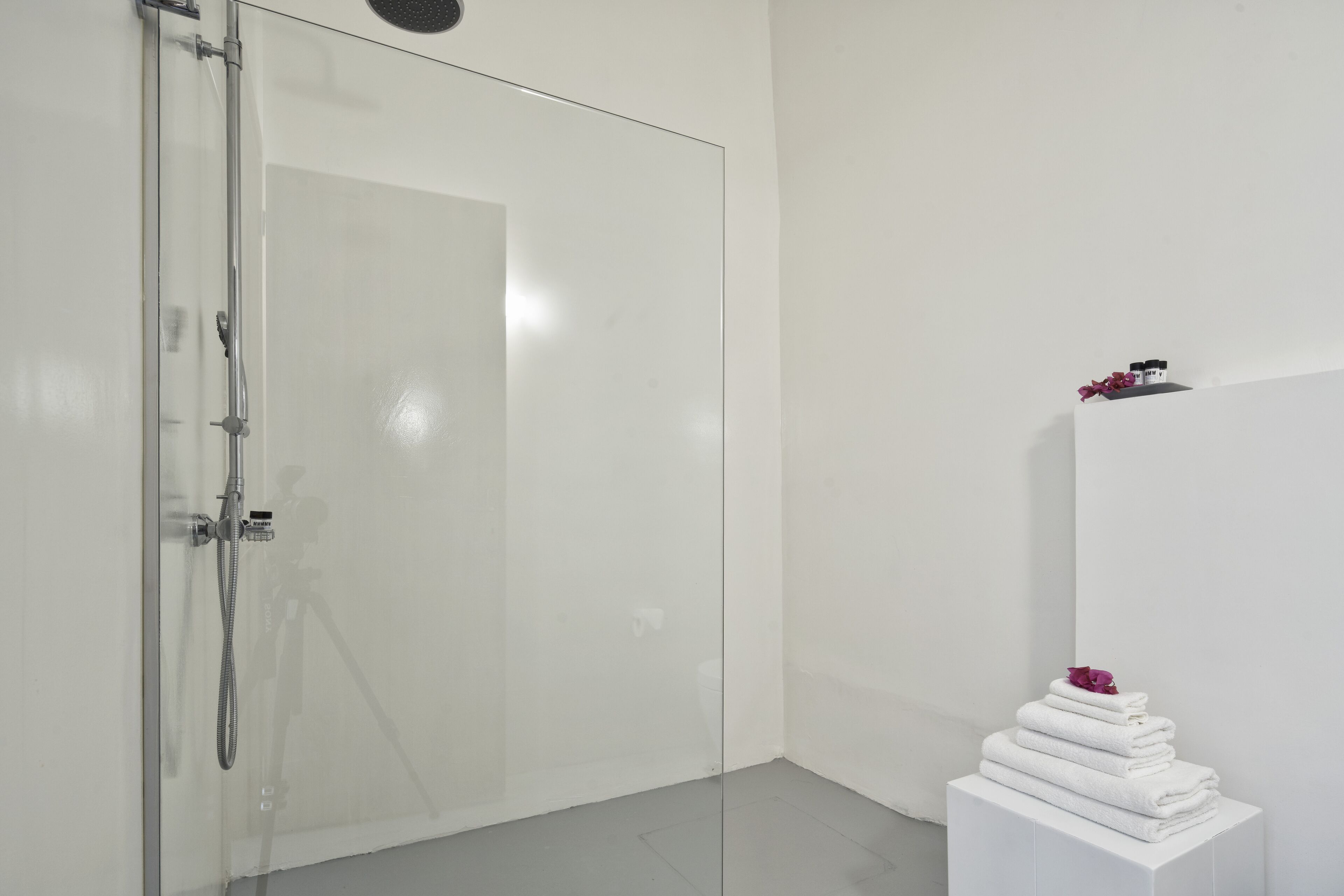 Un baño moderno con cabina de ducha de vidrio, un pedestal blanco con toallas dobladas y un estante pequeño con artículos de tocador.