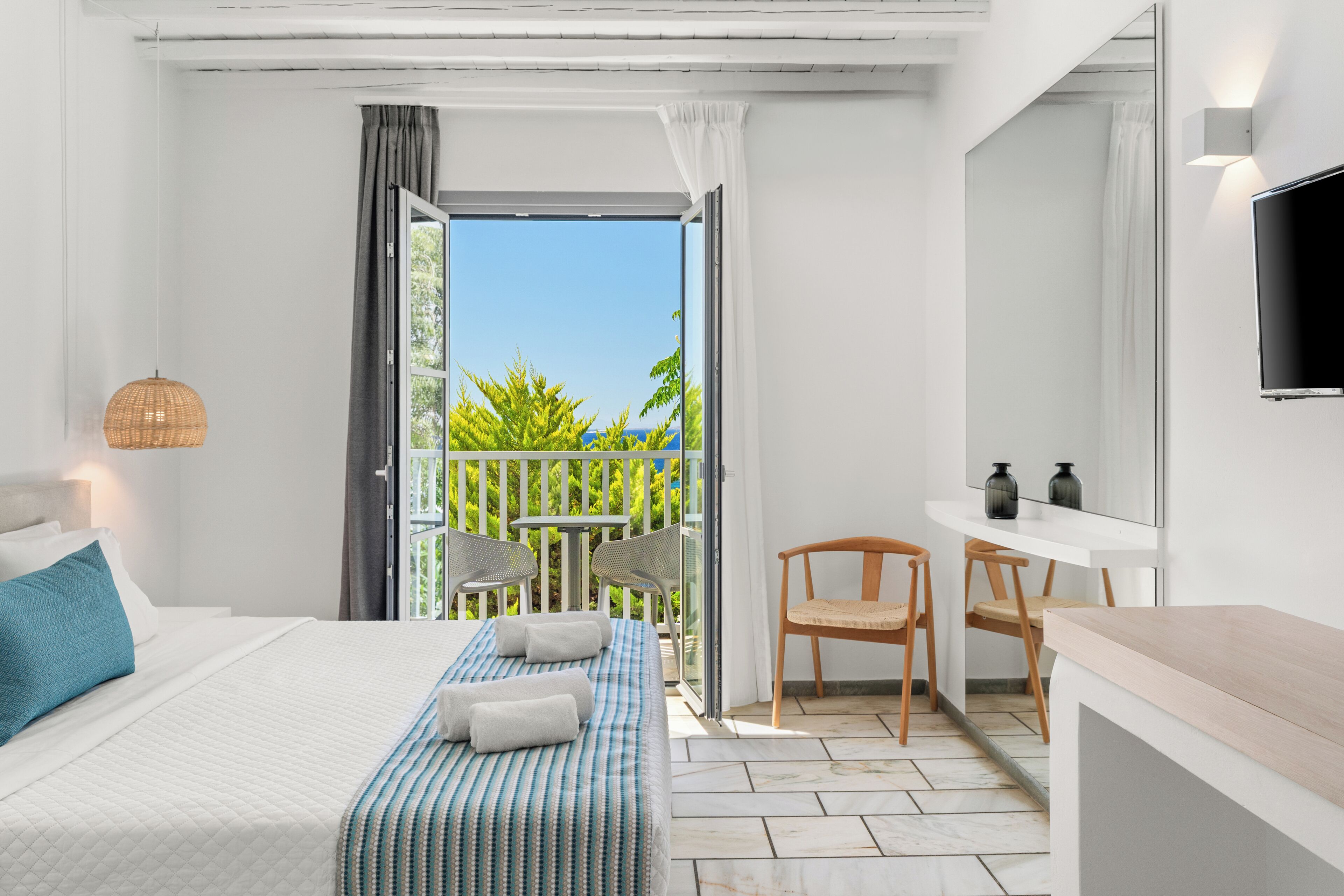 Une chambre d’hôtel équipée d’un lit, d’un bureau, d’une chaise, d’une télévision et d’un balcon donnant sur un espace verdoyant.