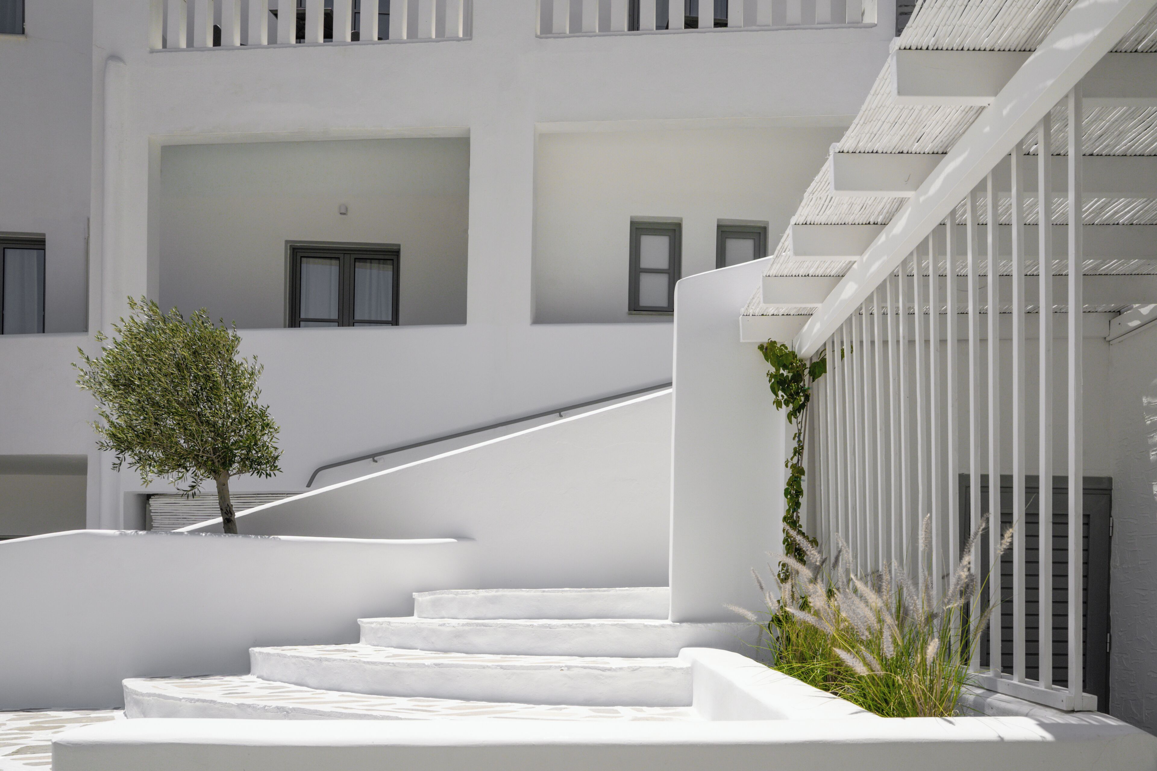 A white staircase leading to a building with multiple windows and a small tree.