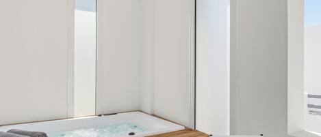 A modern bathroom with a wooden bathtub, a large mirror, and a window providing natural light.