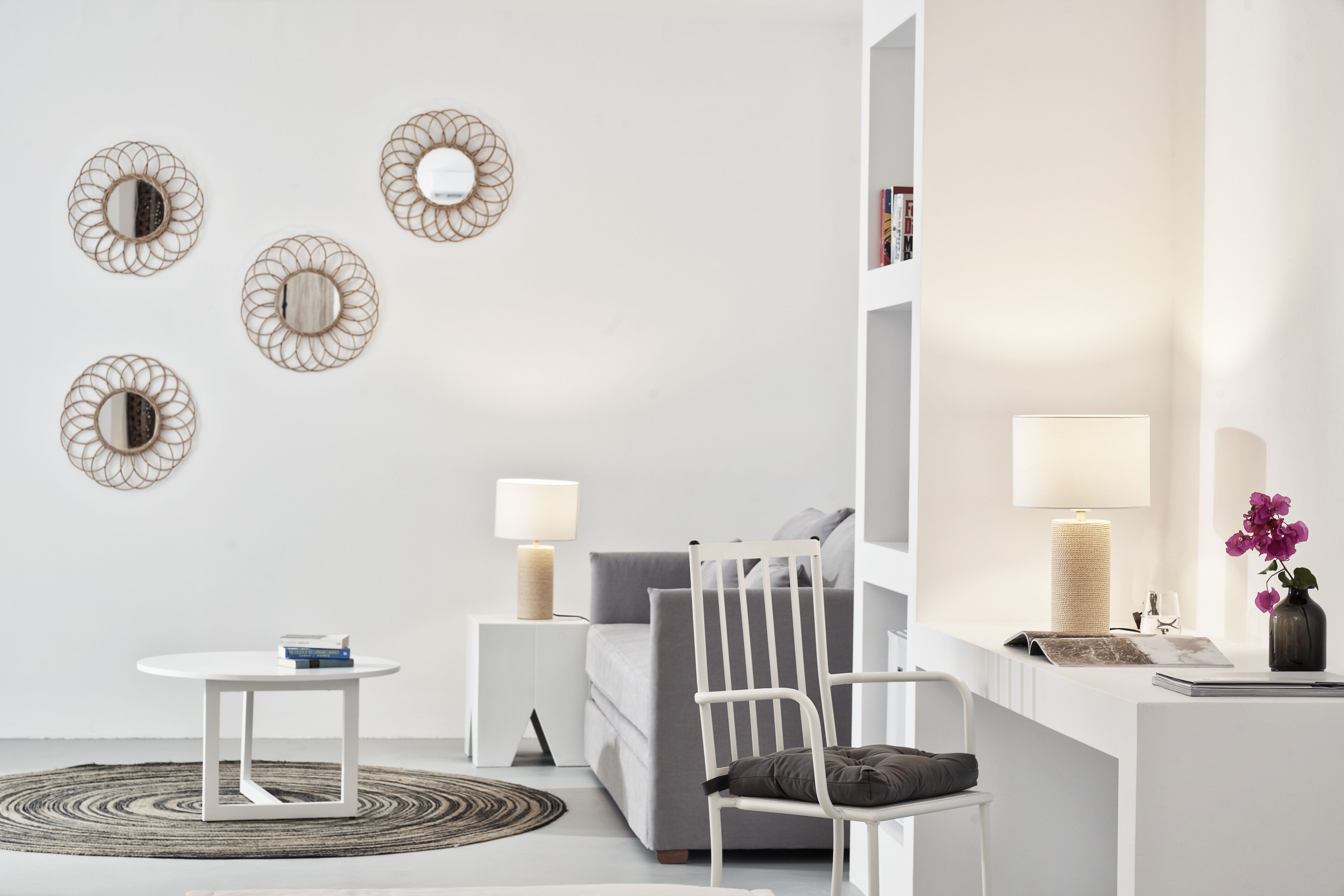 Een moderne woonkamer met een witte bank, een witte stoel, een klein rond tafeltje en een bijzettafeltje met een lamp.