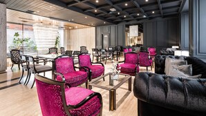 A modern hotel lobby with a mix of seating areas, including a dining table with chairs, a sofa, and a lounge area with chairs.