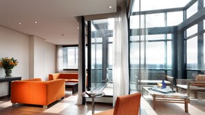 A modern hotel lobby with orange seating, a glass coffee table, and a view of the city through large windows.