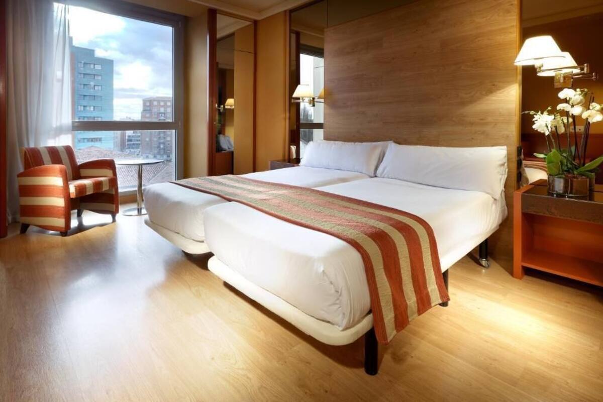 Una habitación de hotel con una cama grande, una silla, una mesita de noche y una lámpara.