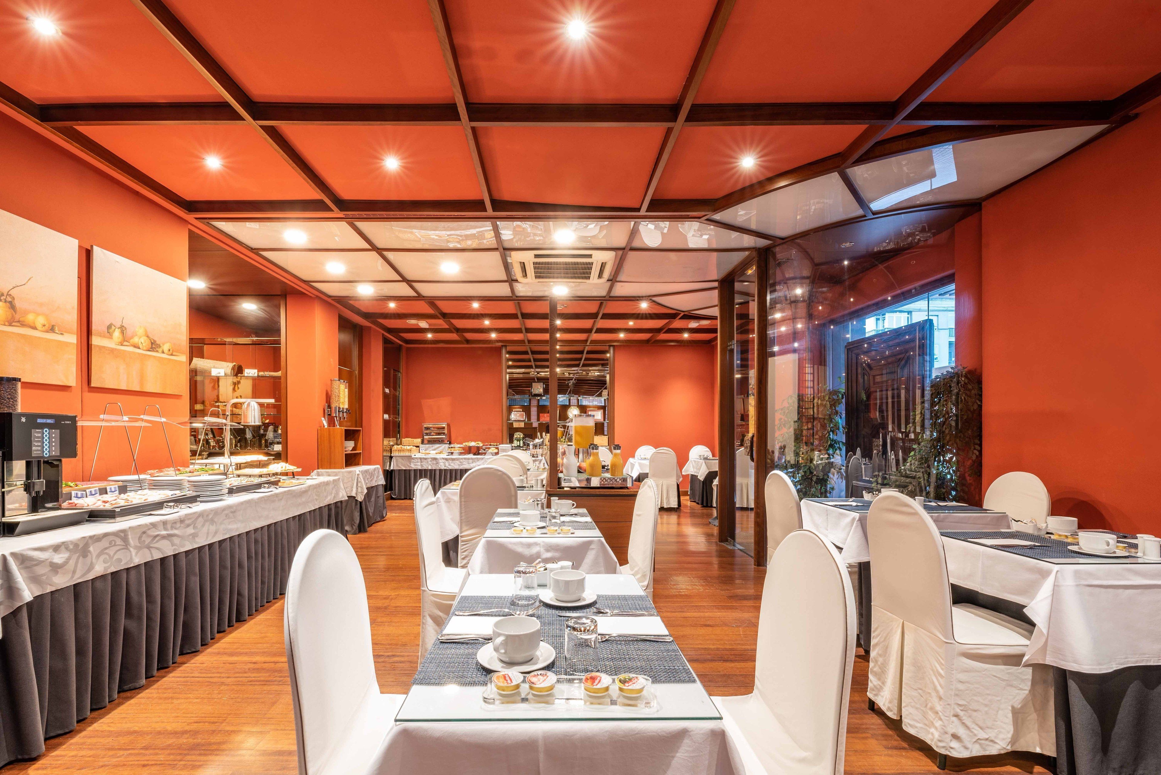 A long dining table with white chairs, a buffet area with food and drinks, and a bright orange interior.