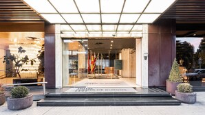 A hotel entrance with a modern design, featuring a glass facade, a metal staircase, and a sign indicating the hotel's name.