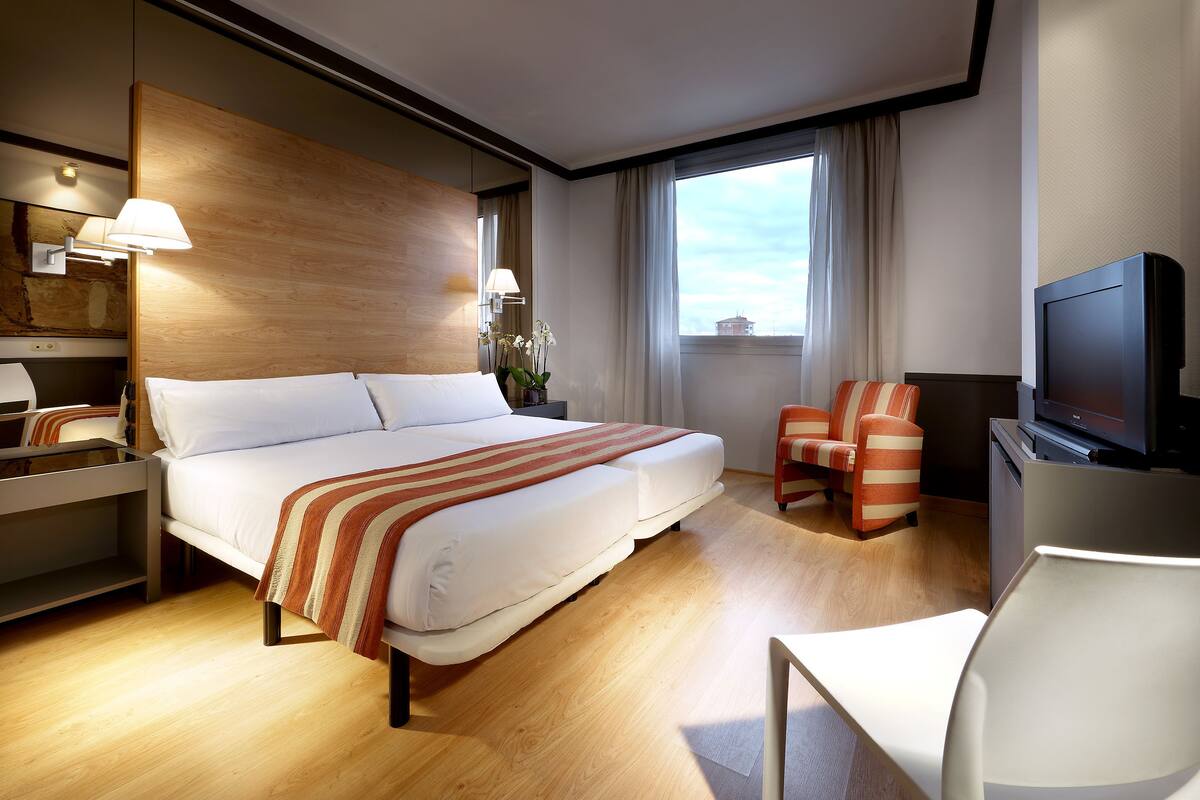 Una habitación de hotel con una cama, televisión, escritorio y una silla.
