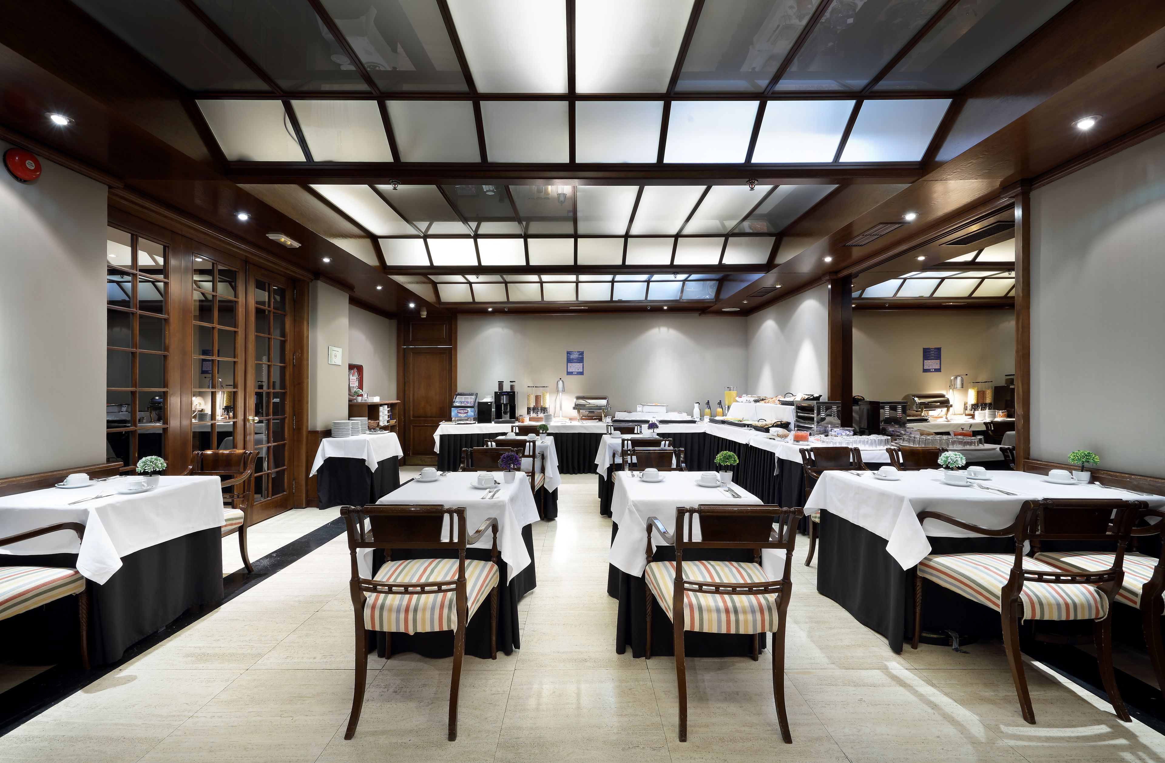 Un espace repas avec plusieurs tables et chaises, une cuisine à l’arrière-plan et un plafond vitré.