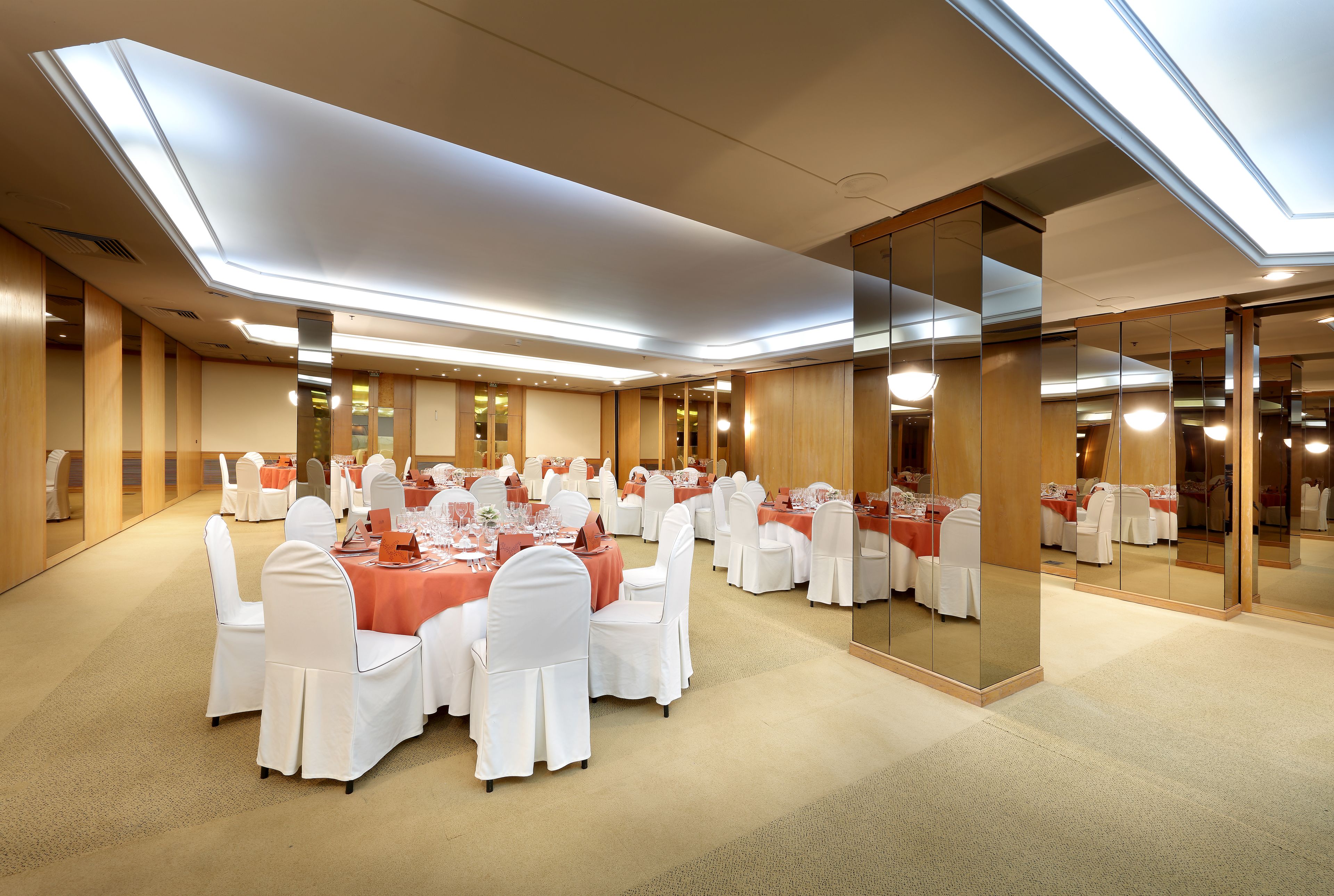 Un salón de conferencias con mesas redondas, sillas blancas y manteles naranja.