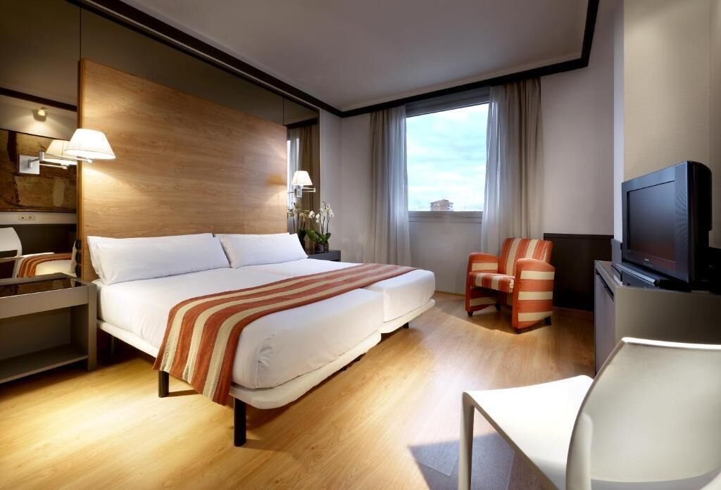 Una habitación de hotel con una cama grande, televisión, escritorio y una silla.