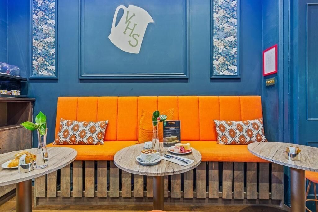A cozy seating area with an orange sofa, two round tables, and a wall-mounted sign reading "YHS".