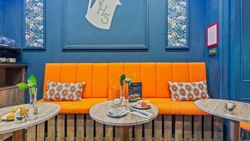 A cozy seating area with an orange sofa, two round tables, and a wall-mounted sign reading "YHS".