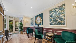 A room with a herringbone floor, green velvet armchairs, a round table, and a large floral painting on the wall. - Vancouver Studios (London)