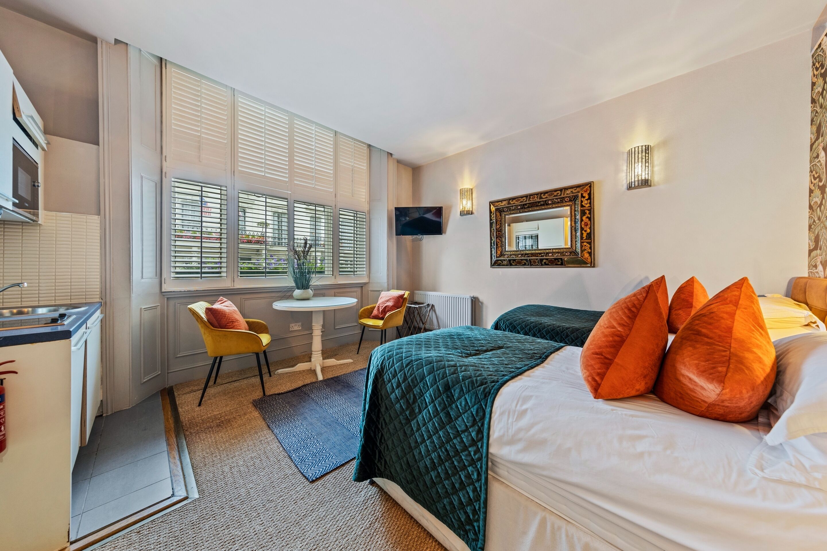 A hotel room with a bed, a desk, a chair, a TV, and a window with blinds.
