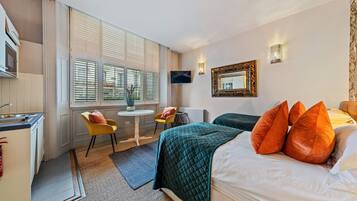 A hotel room with a bed, a desk, a chair, a TV, and a window with blinds.