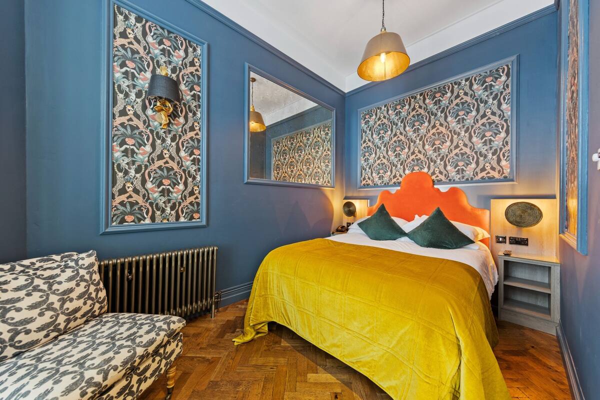 Une chambre à coucher comprenant un lit, une table de chevet, une lampe, un miroir et un radiateur.
