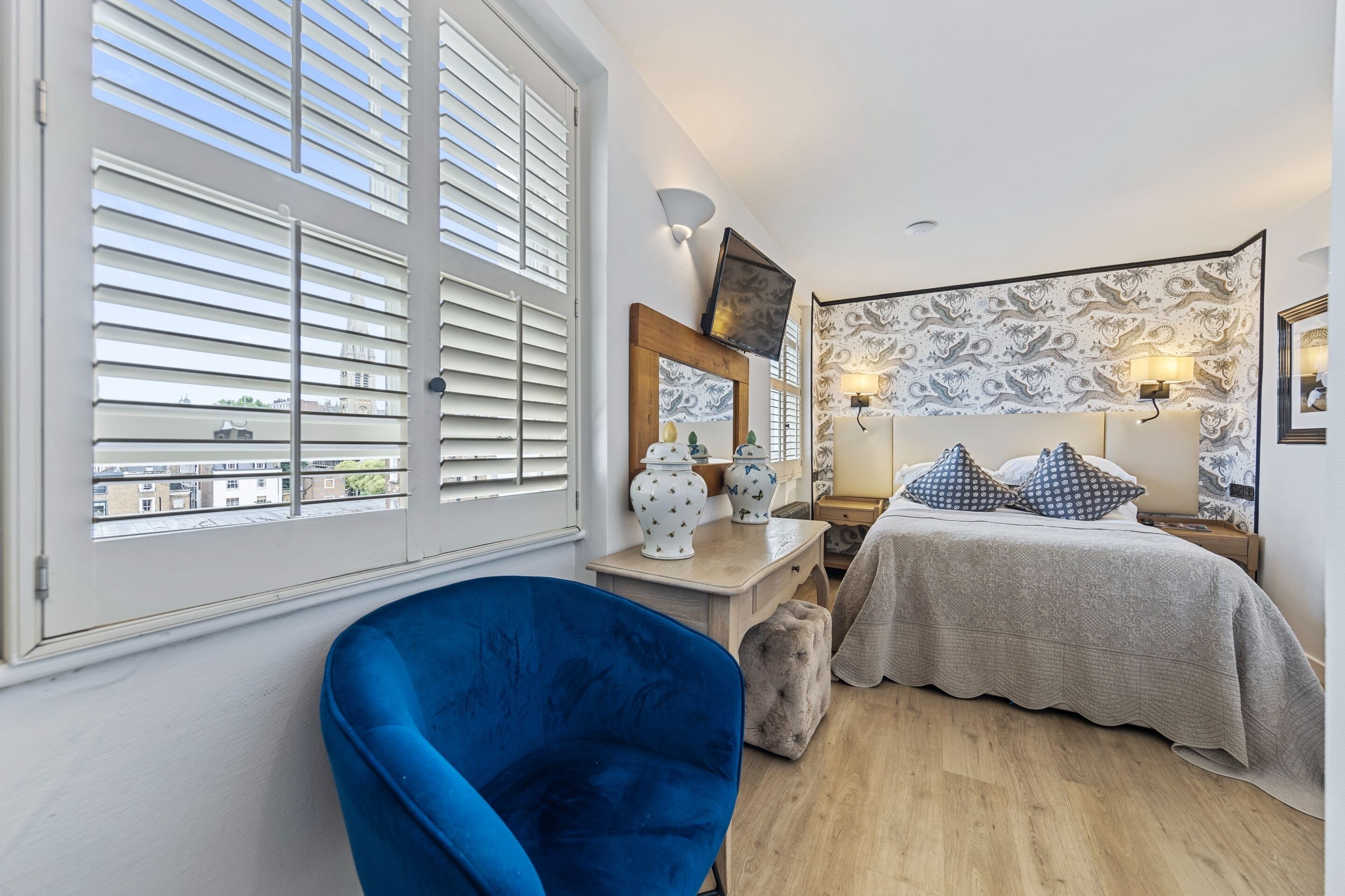 A bedroom with a bed, a dresser, a chair, and a window with blinds.