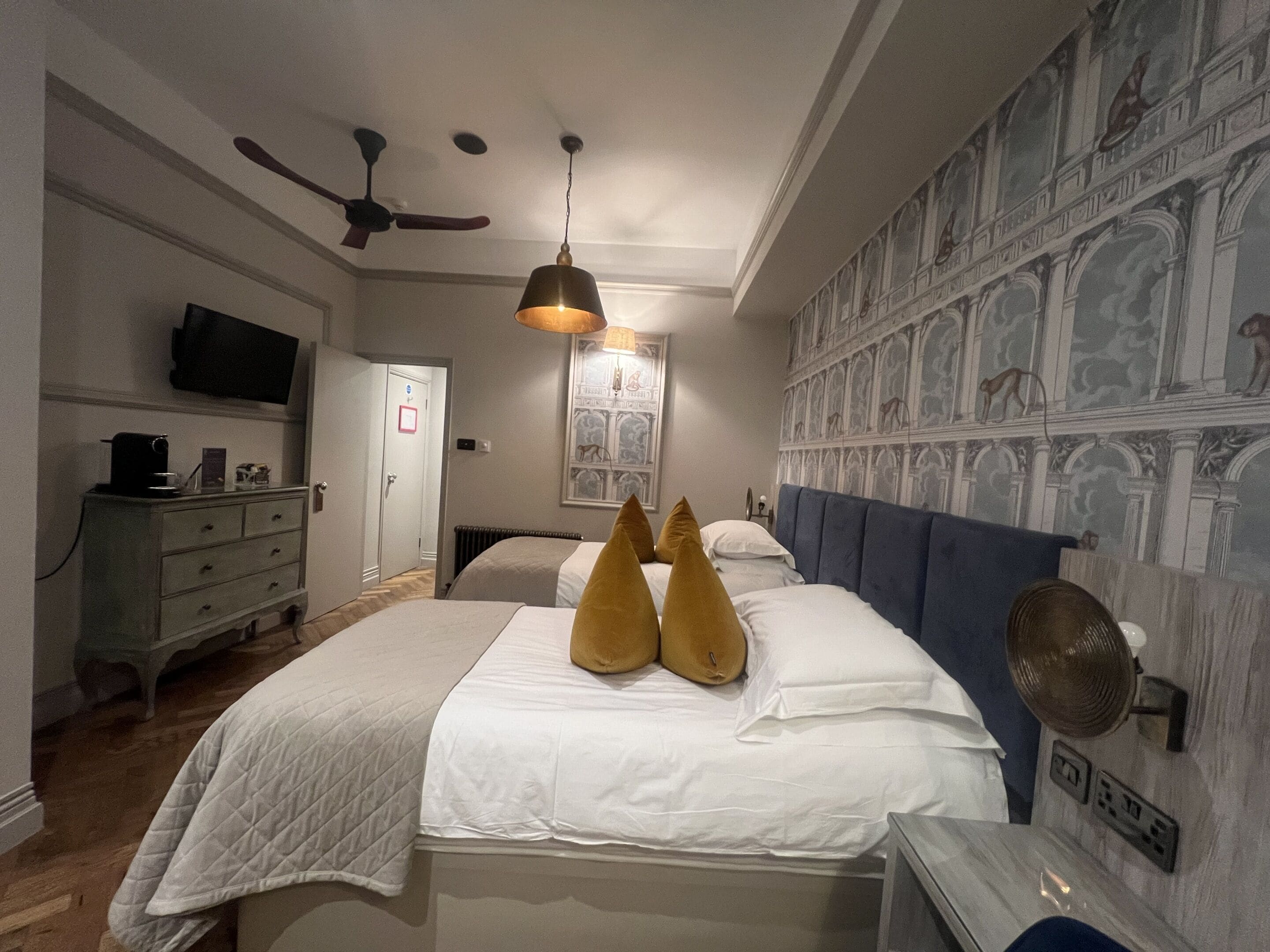 A bedroom with a bed, a ceiling fan, a television, a dresser, and a wall with a patterned design.