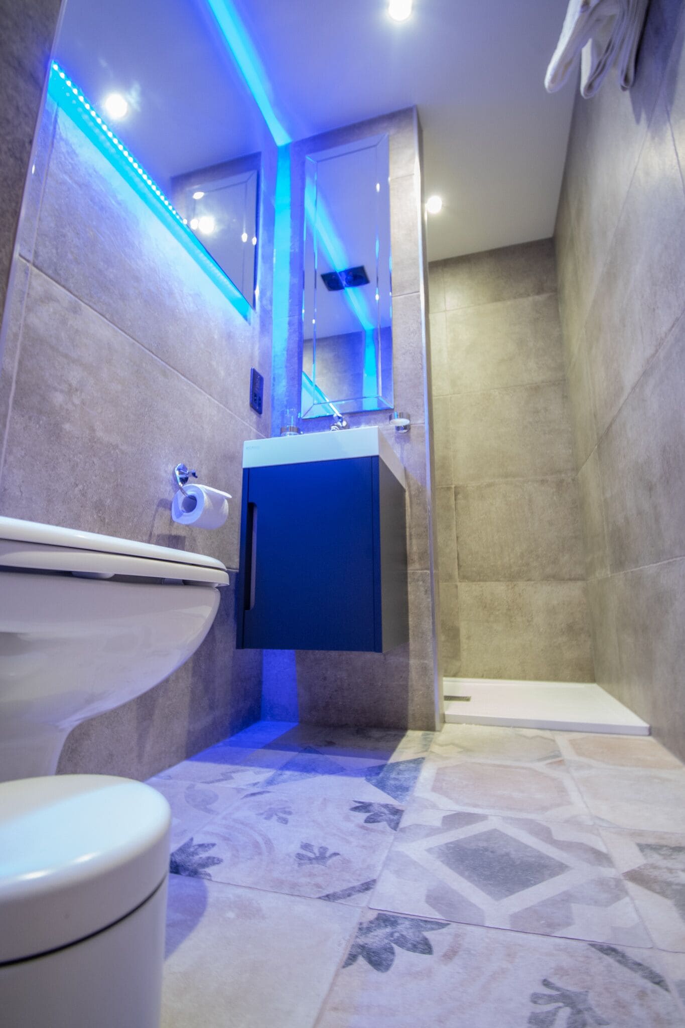 A modern bathroom with a toilet, sink, and shower area, featuring blue LED lighting and patterned tiles.