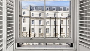 A window with white shutters, revealing a view of a building with multiple windows and balconies. - Vancouver Studios (London)