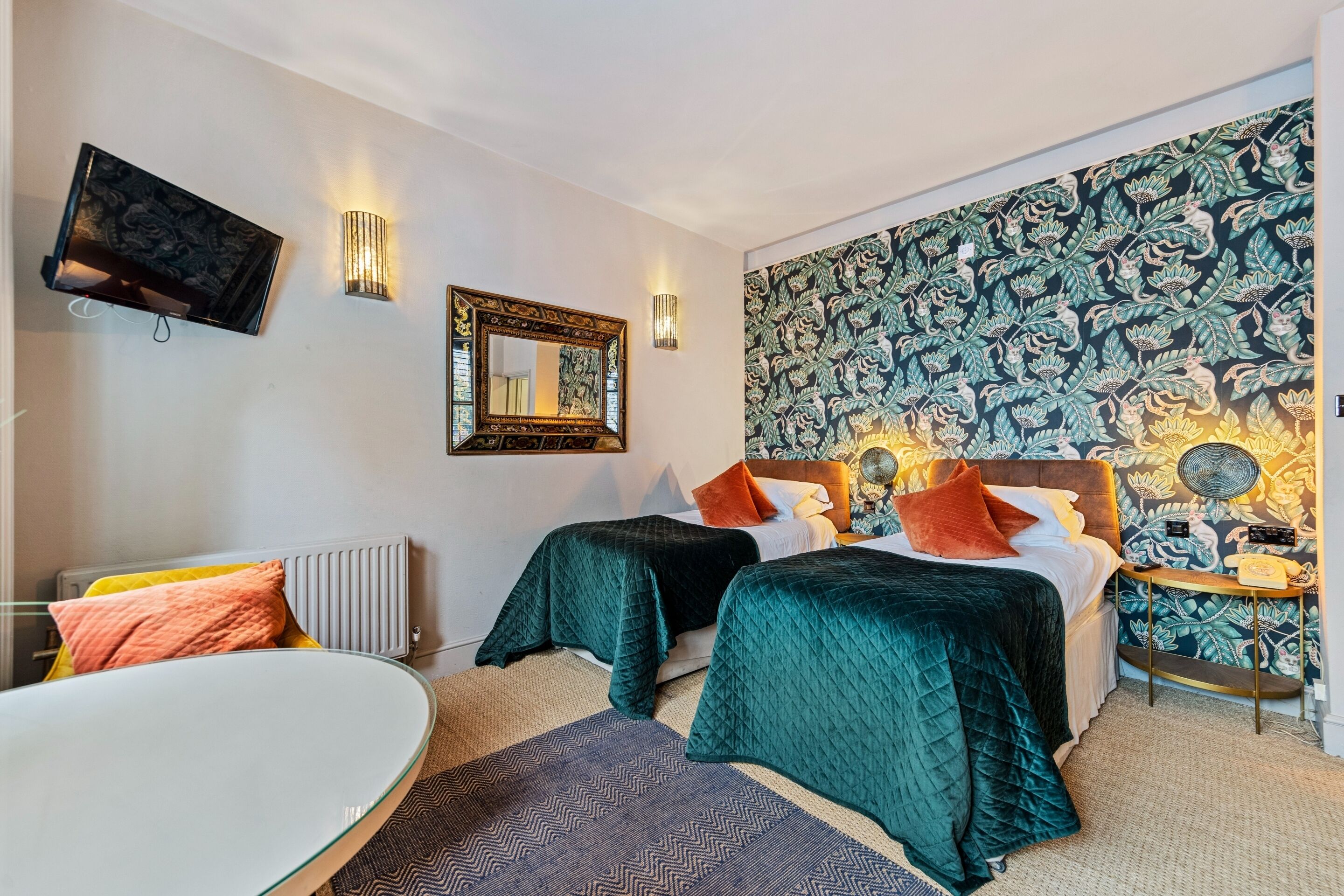 A hotel room with two beds, a round table, a TV, and a patterned wallpaper.