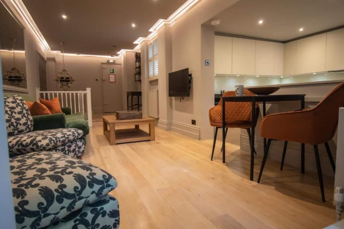 Un salon moderne comprenant un canapé, des fauteuils, une table basse et un coin cuisine avec des placards et un téléviseur.