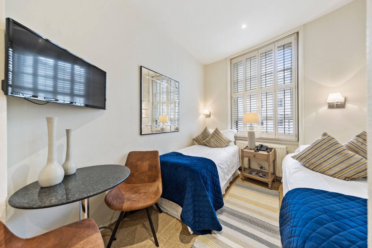 Une chambre d’hôtel équipée d’un lit, d’un bureau, d’une chaise, d’une télévision et d’une fenêtre avec des stores.