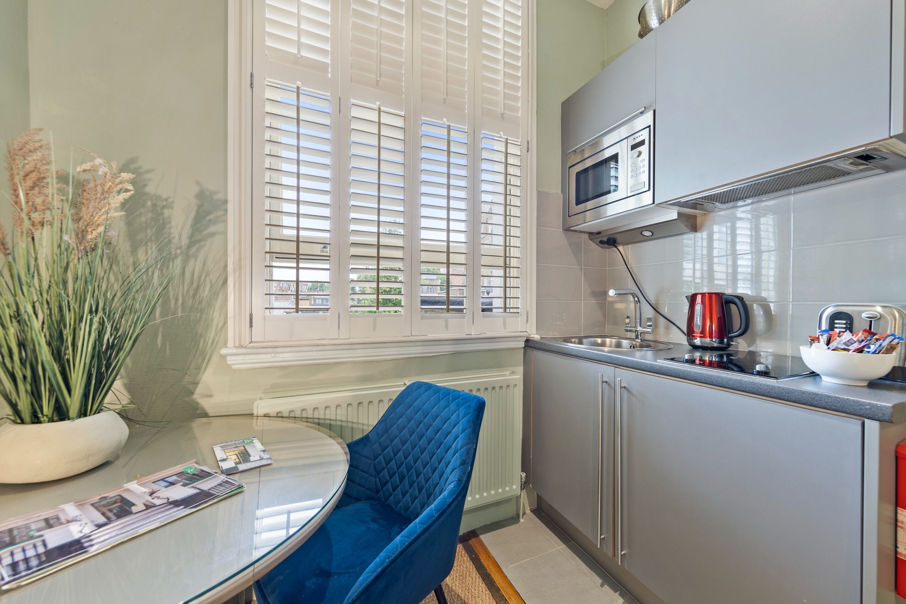 A modern kitchen with a microwave, kettle, and a bowl of snacks on the counter.